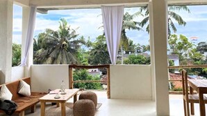 A spacious room with a wooden sofa, a small table, and a view of palm trees and greenery outside. - Wake N Flow, Weligama - Coworking & Coliving (Weligama)