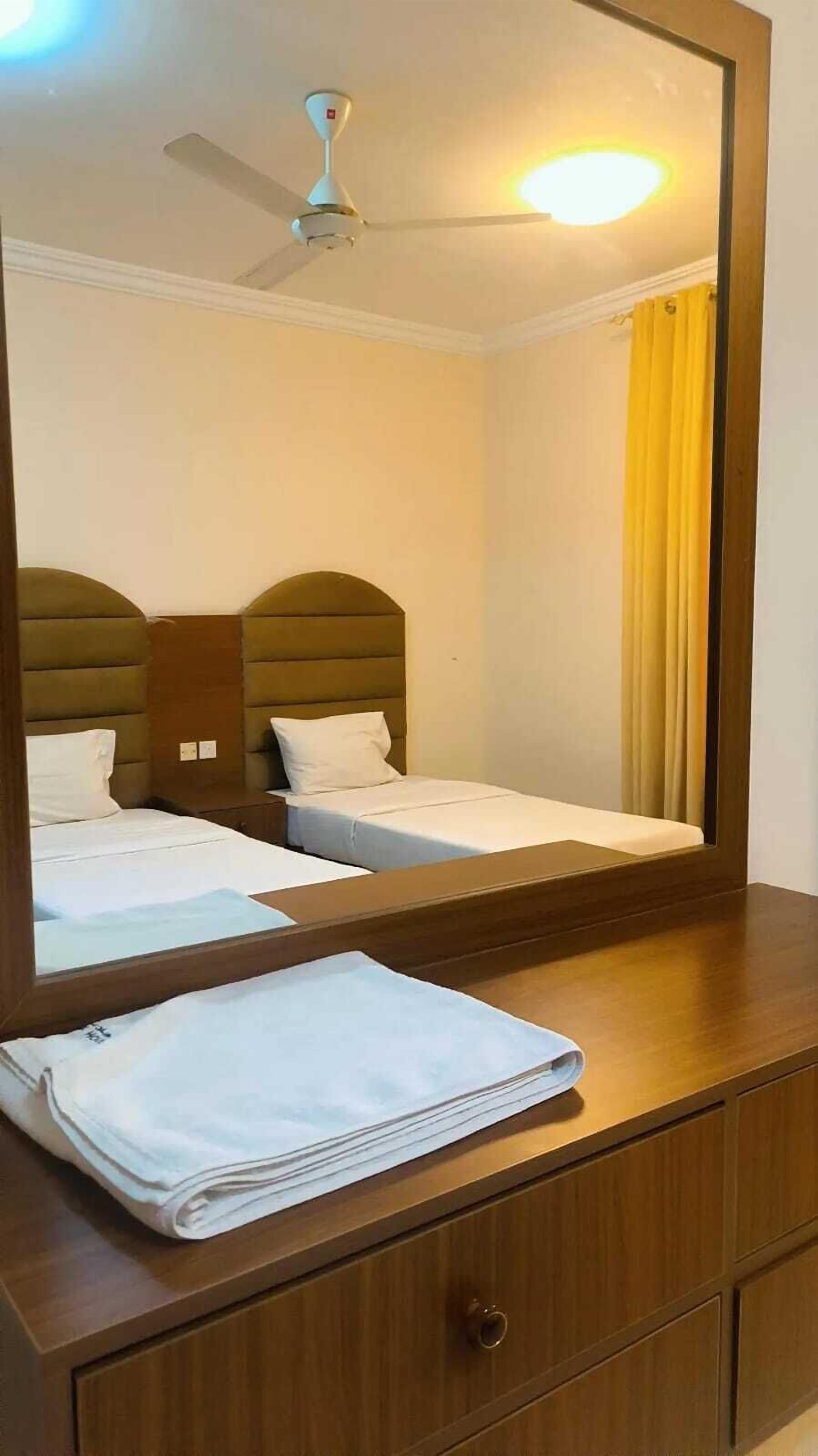 A hotel room with two beds, a wooden dresser, a mirror, and a ceiling fan.