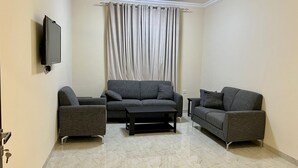 A living room with a grey sofa set, a coffee table, and a flat-screen TV mounted on the wall.