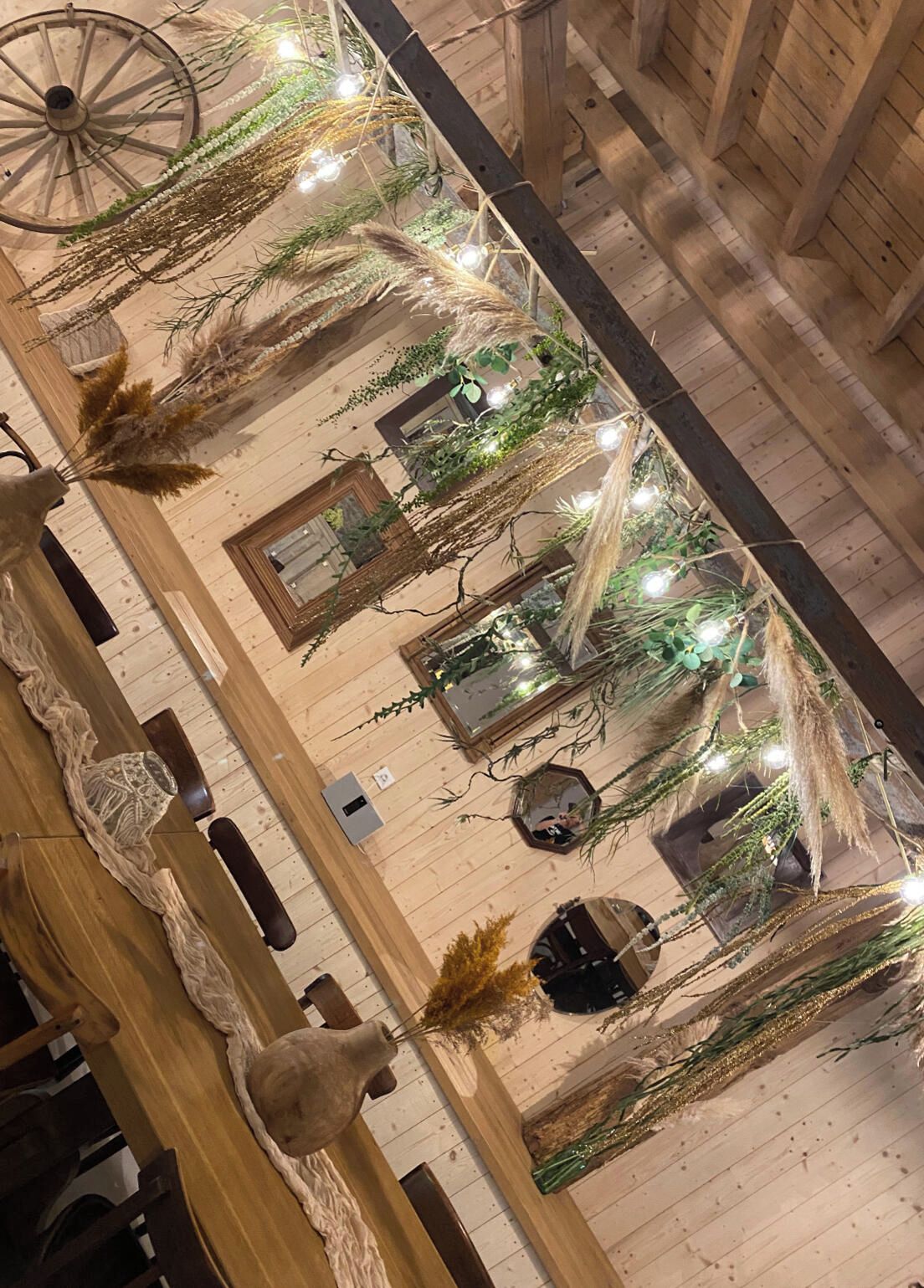 Een kamer met houten wanden, een grote houten tafel, hangende planten en lichtslingers.