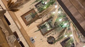 Ein Zimmer mit Holzwänden, einem großen Holztisch, hängenden Pflanzen und Lichterketten.