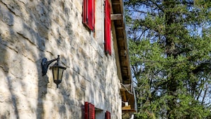 A stone building with red shutters and a wooden deck leading to a gate.