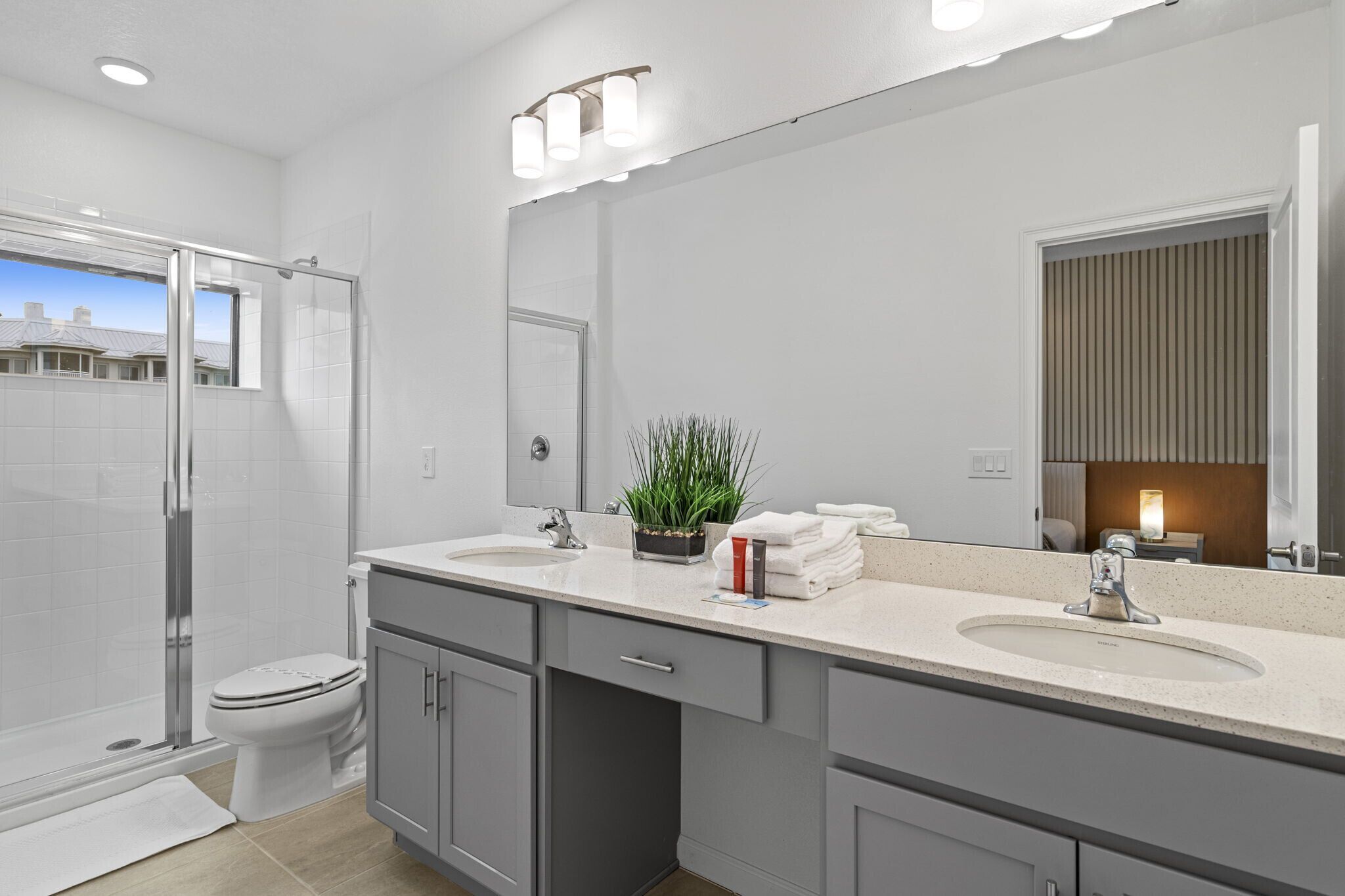 A modern bathroom with a glass shower enclosure, a toilet, a sink with a mirror, and a plant on the counter.