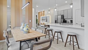 A modern kitchen with white cabinets, a wooden dining table, and bar stools. - Last Minute Disney Getaway! Private Pool & Game Room. Book Now! #118927 (Orlando)