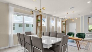 A modern dining area with a white table and grey chairs, a chandelier, and a view of the outside.
