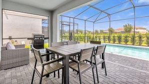 A covered outdoor area with a pool, a barbecue grill, and a table with chairs.
