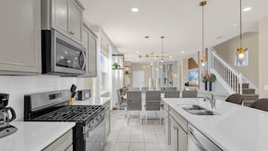A modern kitchen with stainless steel appliances, a central island, and a dining area with grey chairs.