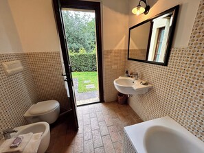 Une salle de bain équipée d’un WC, d’un lavabo et d’une baignoire. Une fenêtre donne sur un jardin.