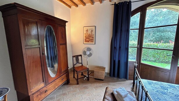 Une pièce comprenant un meuble en bois, une chaise, un ventilateur, une fenêtre avec des rideaux et un banc avec des serviettes.