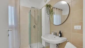Een badkamer met een douchecabine van glas, een witte wastafel en een spiegel aan de muur.