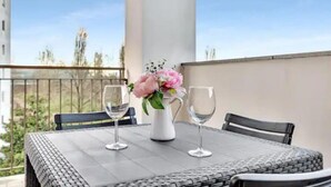 Een balkon met een tafel gedekt voor twee personen, twee wijn glazen en een vaas met bloemen.