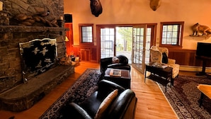 A cozy living room with a stone fireplace, leather sofas, and deer antlers mounted on the wall. - Camp Bear Claw, private home on the shores of Oseetah Lake.  (Saranac Lake)