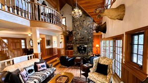 A spacious living area with a fireplace, wooden furniture, and a stone wall. - Camp Bear Claw, private home on the shores of Oseetah Lake.  (Saranac Lake)