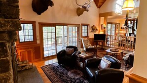 A spacious living room with a stone fireplace, leather sofas, a patterned rug, and large windows. - Camp Bear Claw, private home on the shores of Oseetah Lake.  (Saranac Lake)