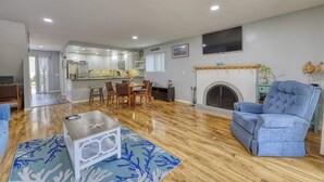 A spacious living area with a dining table, blue armchair, and a fireplace. - 28 Sol Vista Complex - Spacious, Deck, BBQ, Common Pool + GOLF CART (Avalon)