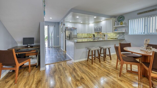 A modern kitchen with a central island, wooden flooring, and a dining area with a round table and chairs. - 28 Sol Vista Complex - Spacious, Deck, BBQ, Common Pool + GOLF CART (Avalon)