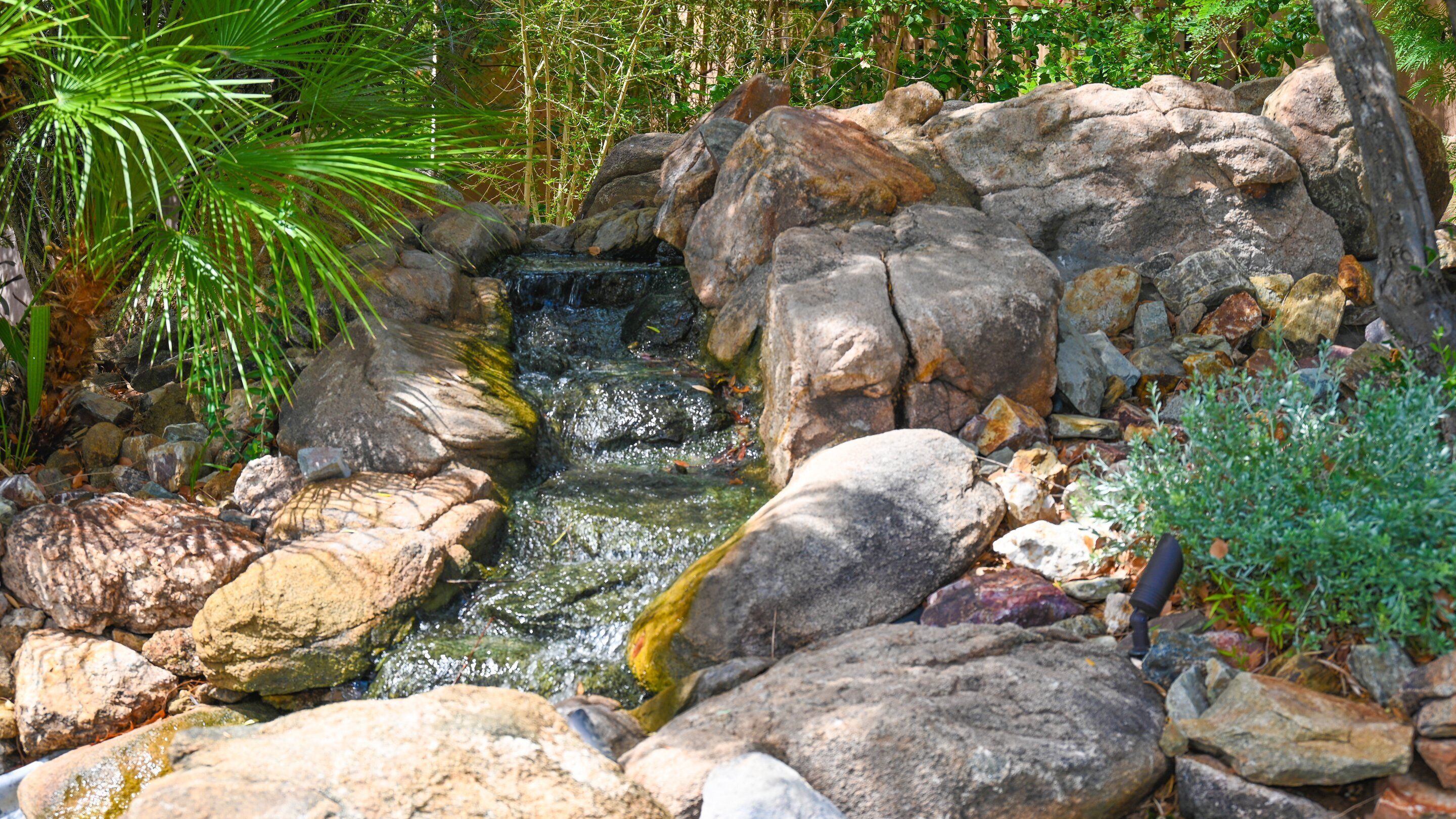 A small waterfall surrounded by large rocks and greenery.