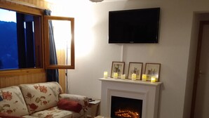 A cozy living room with a fireplace, a flat-screen TV, and a floral sofa. - Magnificent panorama (Le Biot)