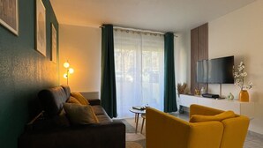 Un salon moderne avec un canapé, un fauteuil jaune, une petite table ronde et un téléviseur posé sur un meuble.