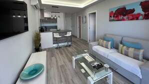 A modern living room with a glass coffee table, a sofa with patterned cushions, and a kitchen area with a bar. - Boutique one bed sea views free wifi (Arona)