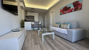 A modern living room with a grey sofa, a glass coffee table, and a kitchen area in the background. - Boutique one bed sea views free wifi (Arona)