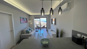 A modern living room with a sofa, a dining table, and a view of the sea through large windows. - Boutique one bed sea views free wifi (Arona)