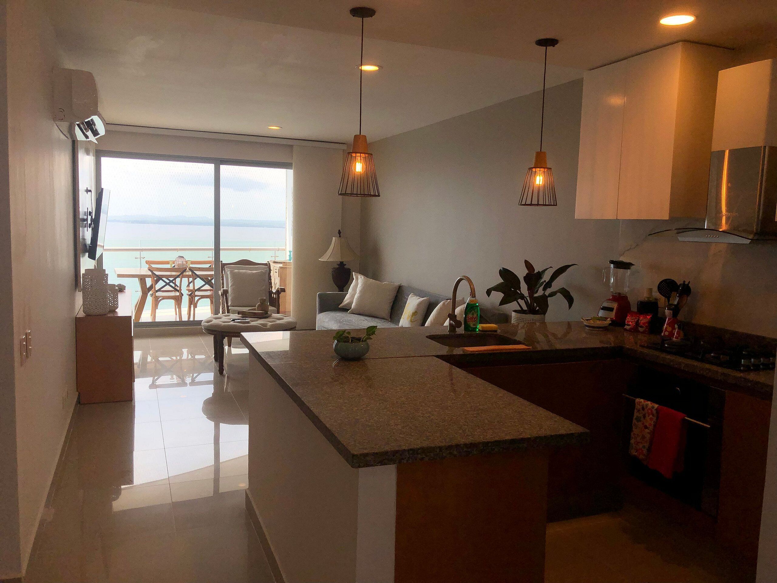 Uma cozinha moderna com uma ilha central, luminárias pendentes e vista para o mar através de uma grande janela.