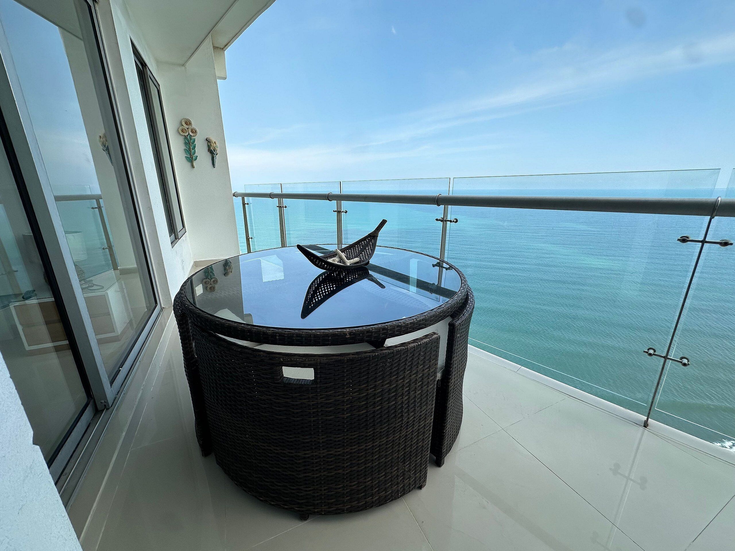 Ein runder Tisch mit Glasplatte, dekoriert mit einem Seestern, auf einem Balkon mit Glasgeländer und Blick aufs Meer.