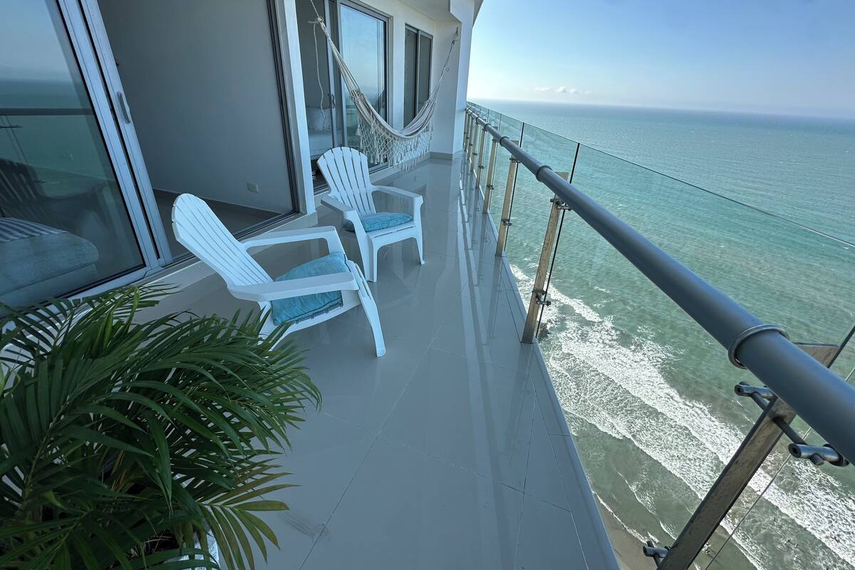 Een balkon met witte stoelen en een hangmat, met uitzicht op de oceaan.