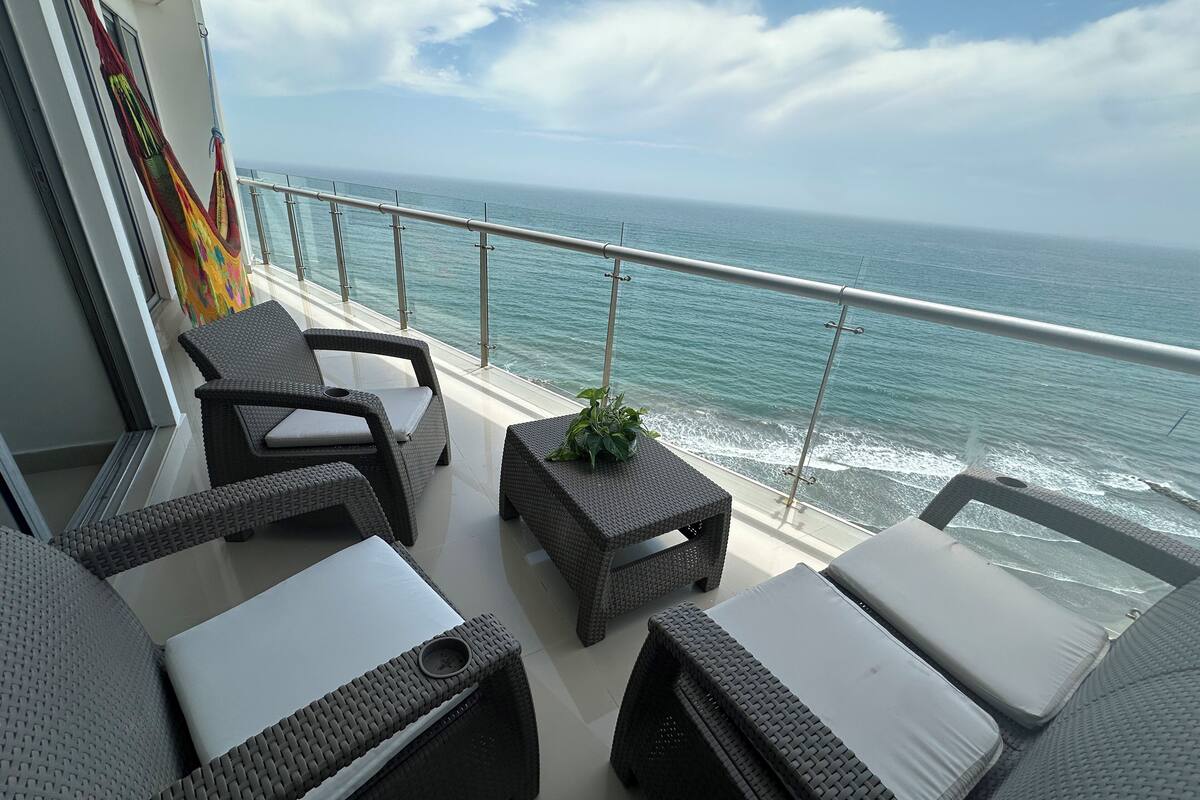Een balkon met rieten meubilair, een bloempot en uitzicht op zee.