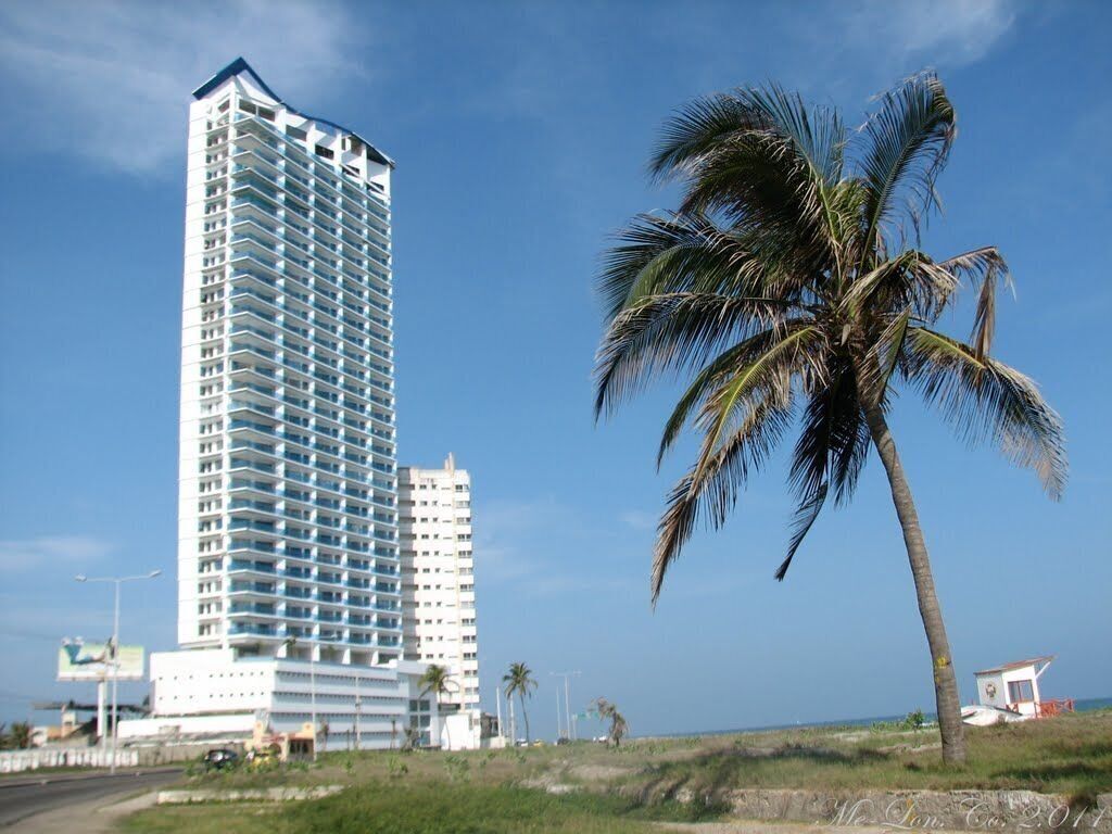 A tall, multi-story hotel with a modern design, located near a beach with palm trees.