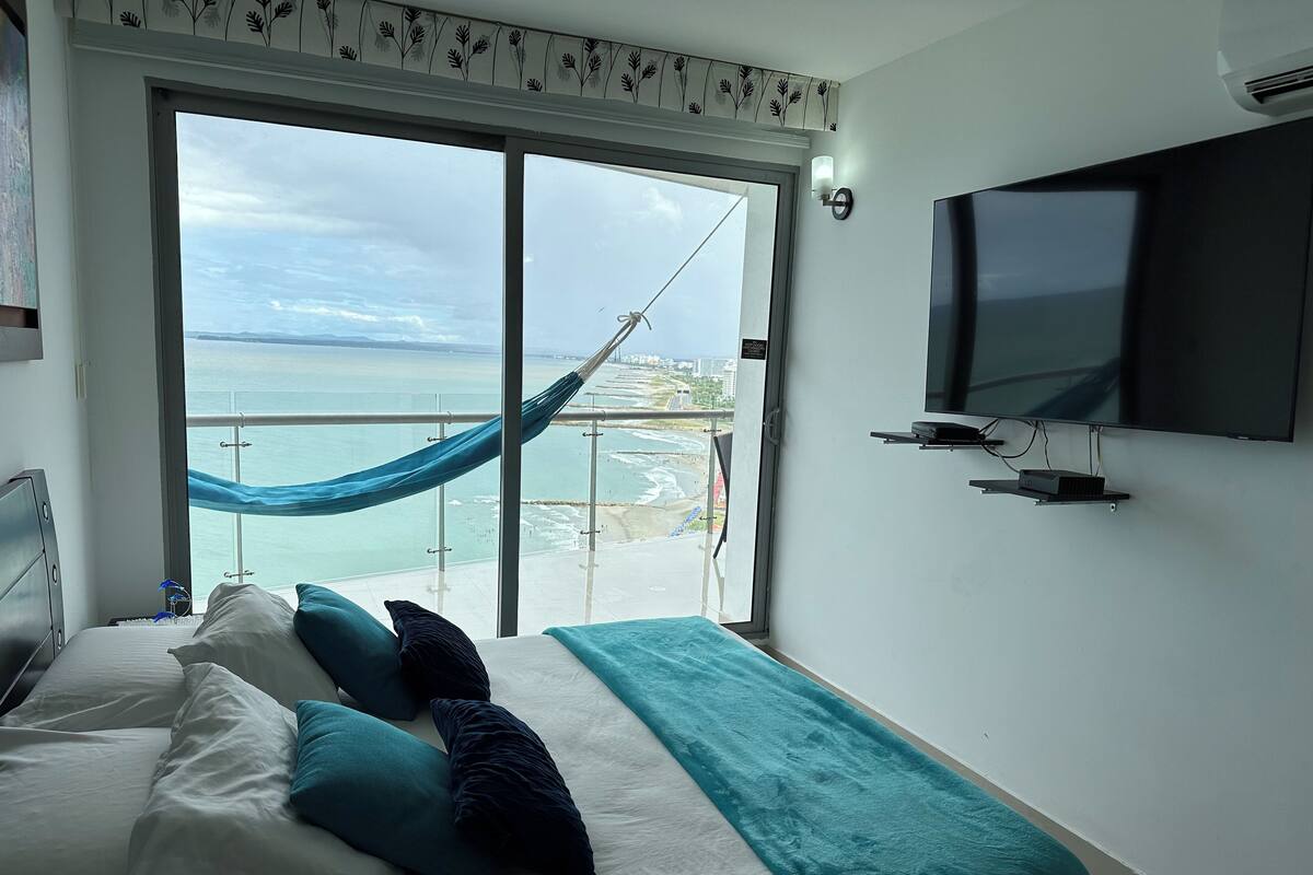 Een hotelkamer met een bed, een televisie en een balkon met uitzicht op zee.