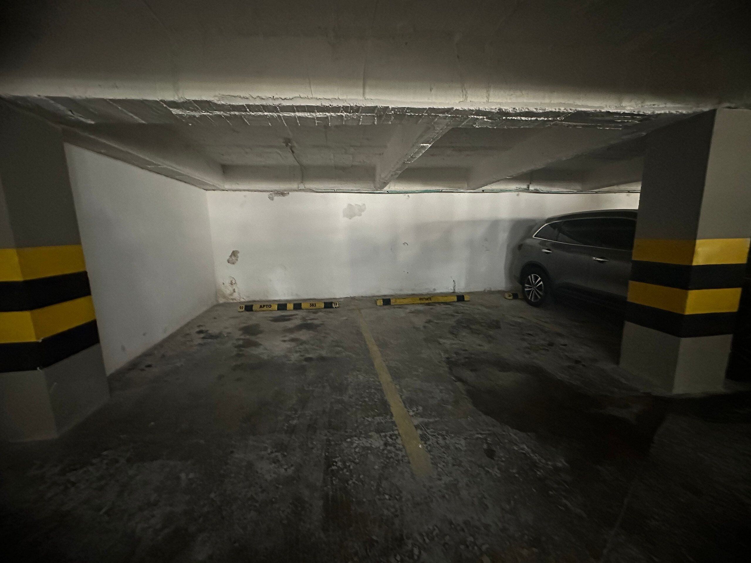 Un estacionamiento subterráneo tenuemente iluminado, con pilares de hormigón y un automóvil estacionado en una de las plazas.