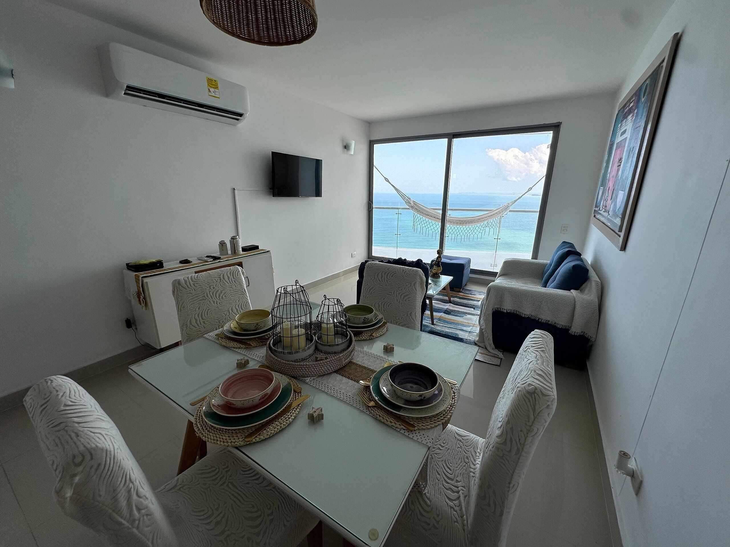 A dining area with a table set for four, a sofa, and a large window with a view of the sea.
