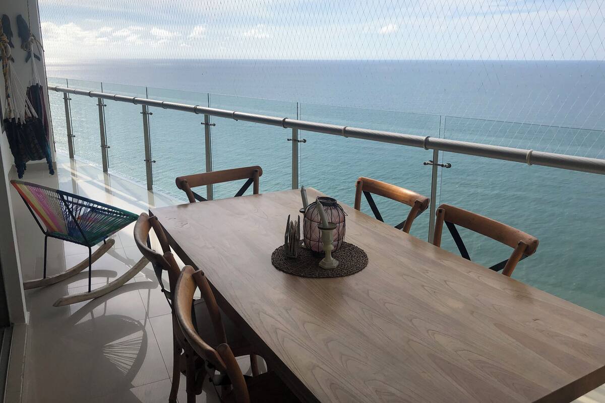 Een houten tafel met stoelen op een balkon met uitzicht op zee.