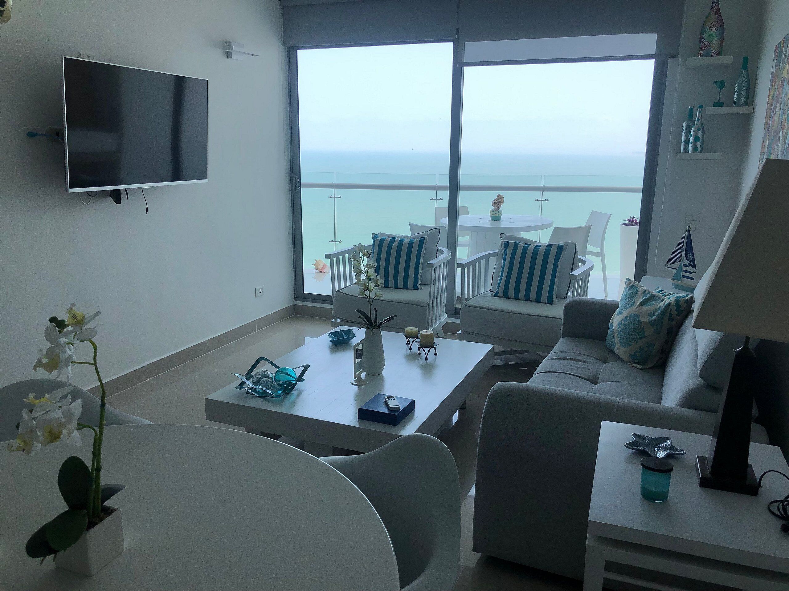 Uma sala de estar moderna com varanda, televisão de tela plana e vista para o mar.