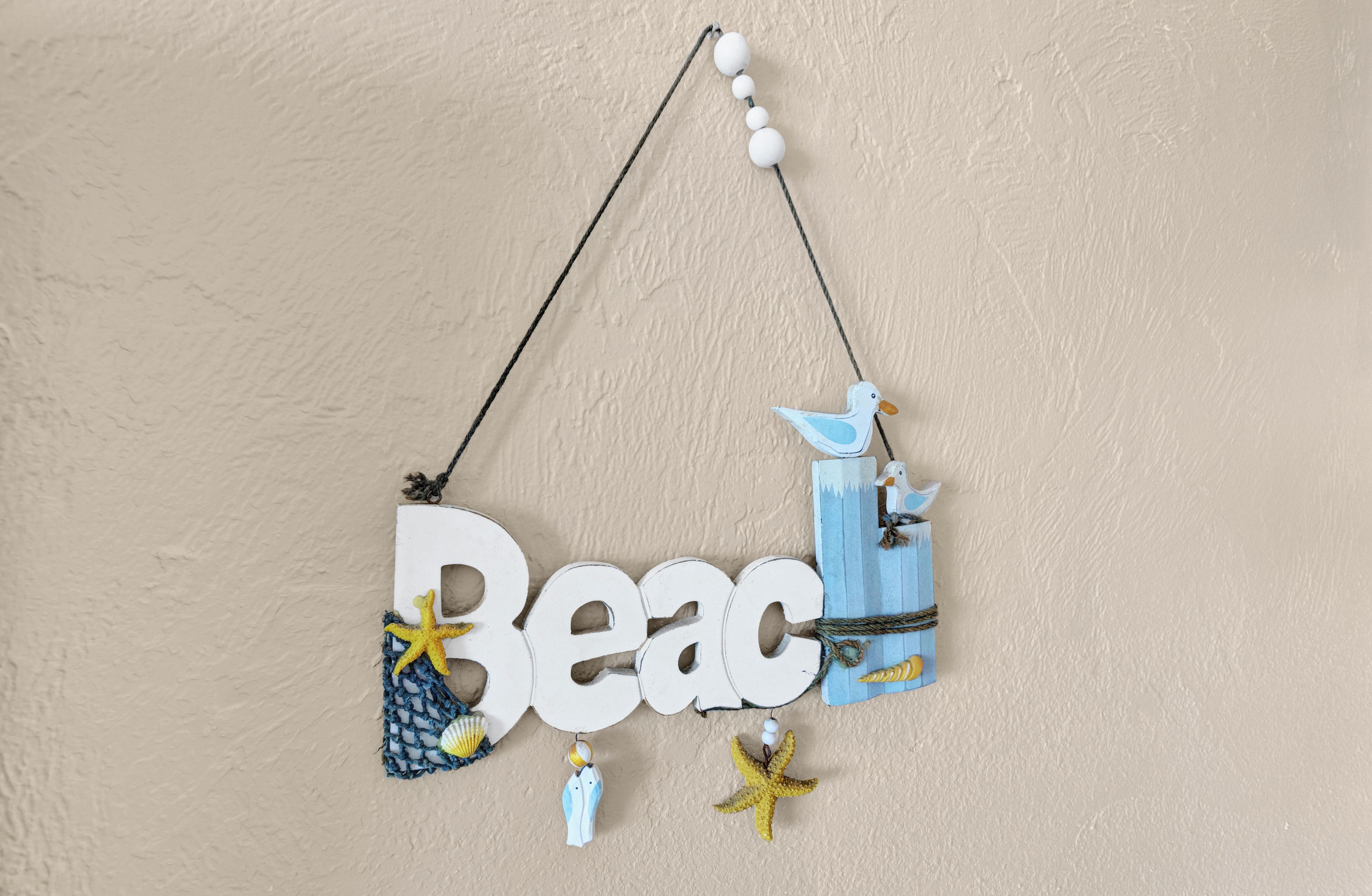 Decoración de pared con la palabra "Beac" y diversos elementos marinos como una estrella de mar, un adorno con forma de estrella de mar y una botella azul.