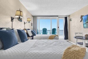 A hotel room with two beds, a balcony with chairs, and a table with chairs.