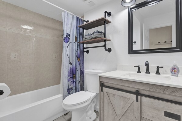A bathroom with a shower, toilet, sink, and a mirror.