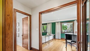 Een ruime kamer met houten vloeren, een piano, een bank en een raam met gordijnen.