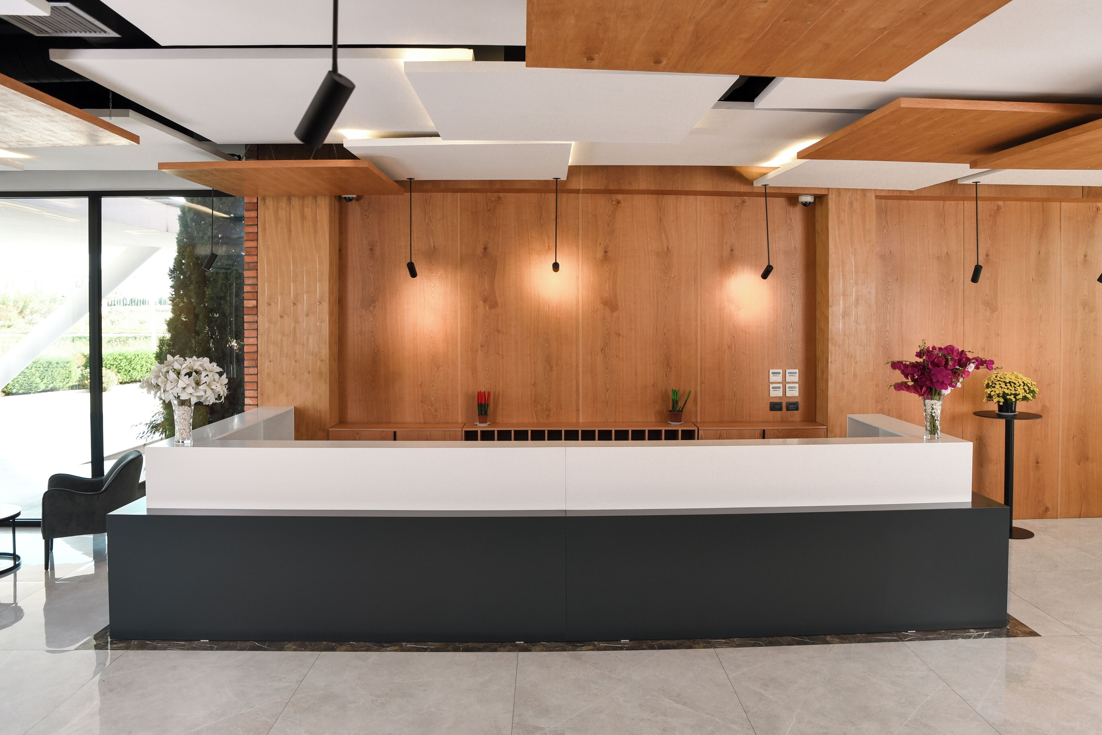 Un mostrador de recepción de diseño moderno, paneles de madera en las paredes y un amplio ventanal con vistas a zonas verdes.