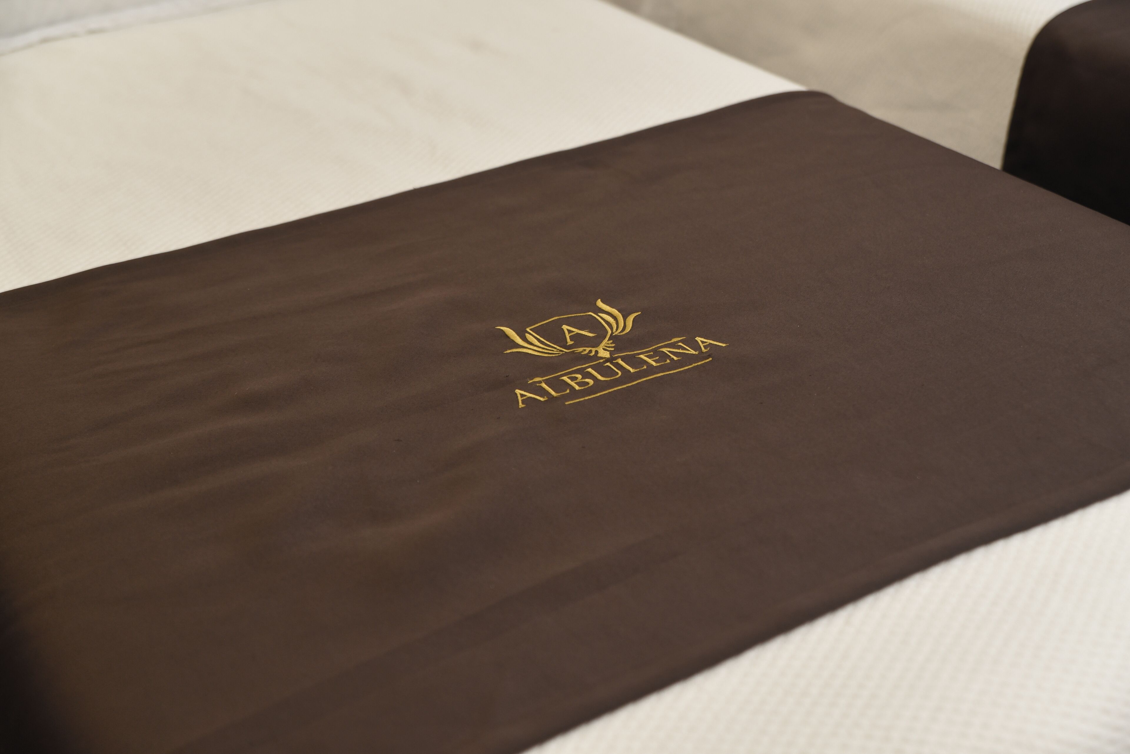 A brown, textured surface with a gold emblem and the text "AUBULENA" in gold lettering.