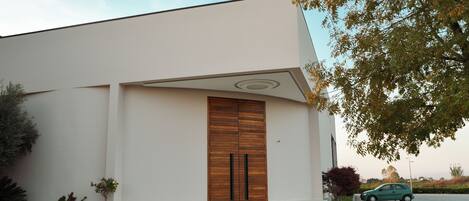 A modern building with a large wooden door, a paved entrance, and a car parked nearby.