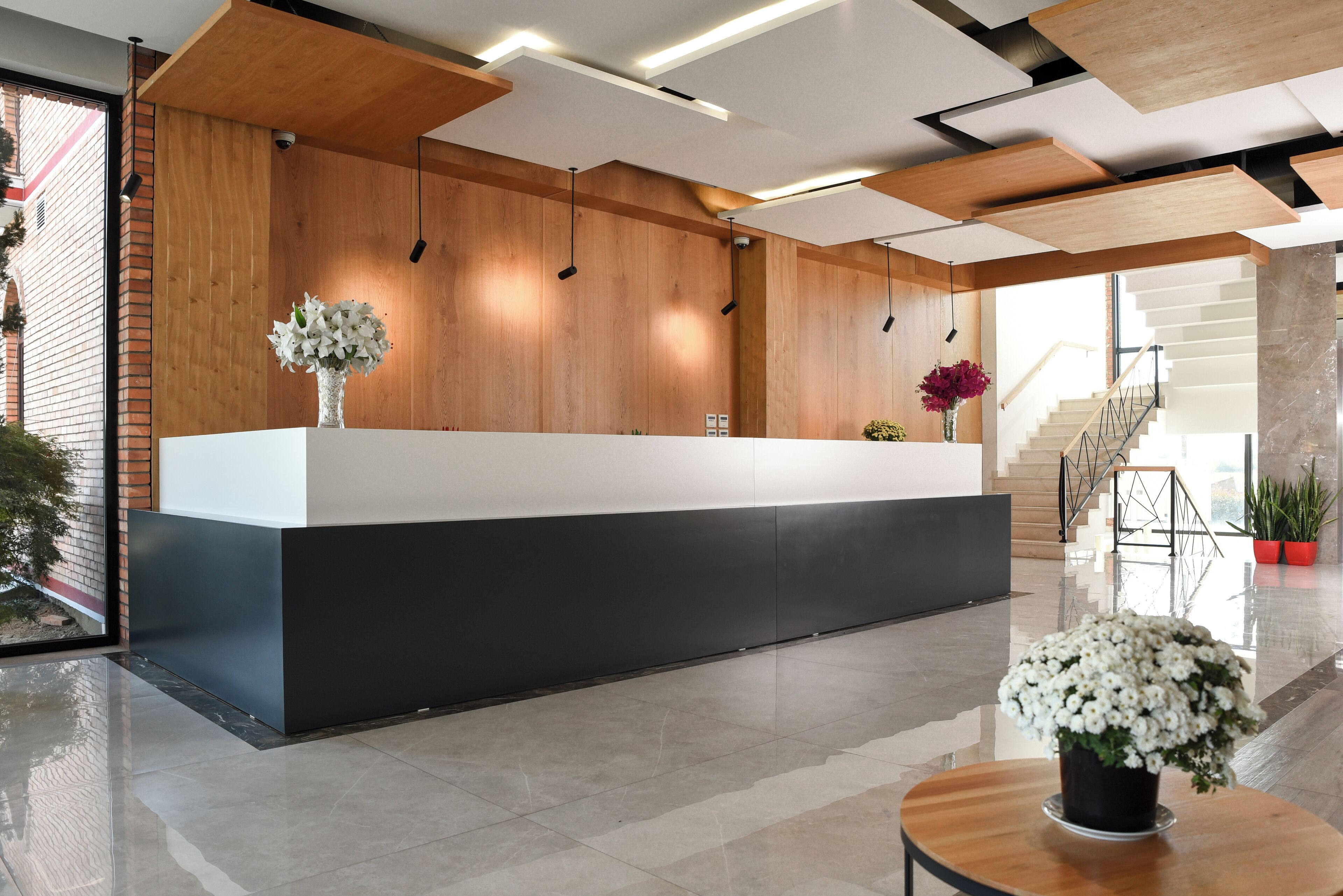 Un mostrador de recepción moderno con un panel de pared de madera, una barra negra y una planta en maceta.