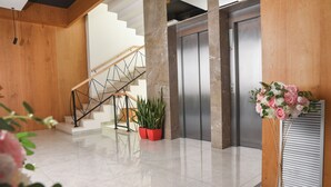 A modern lobby with a staircase, elevators, and potted plants. - Hotel Albulena (Mamurras)