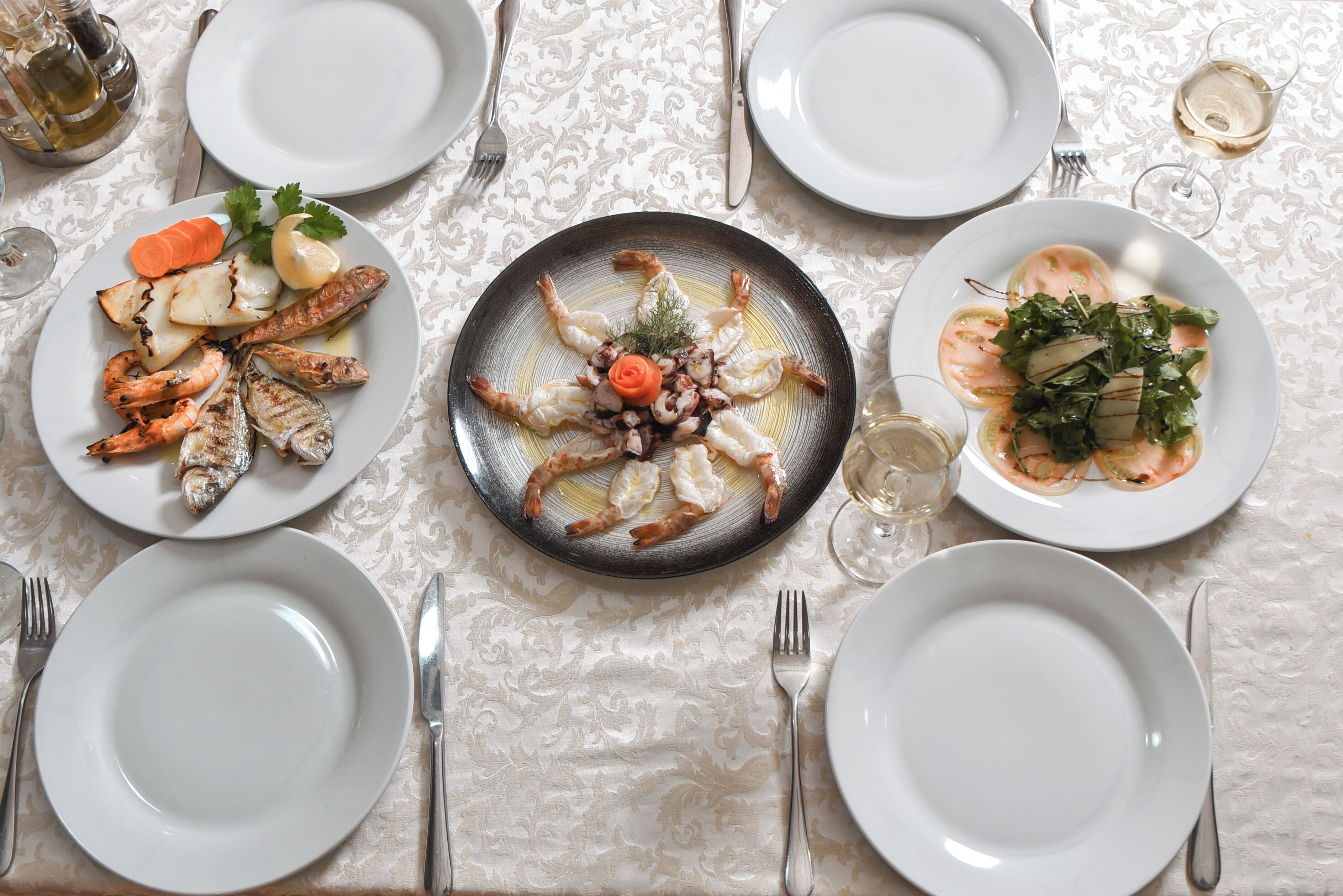 A table set with plates of seafood, glasses of wine, and cutlery.