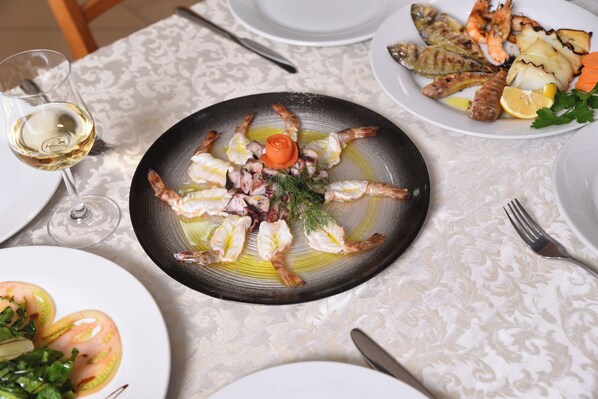 A dining table with plates of seafood, a glass of white wine, and a fork.