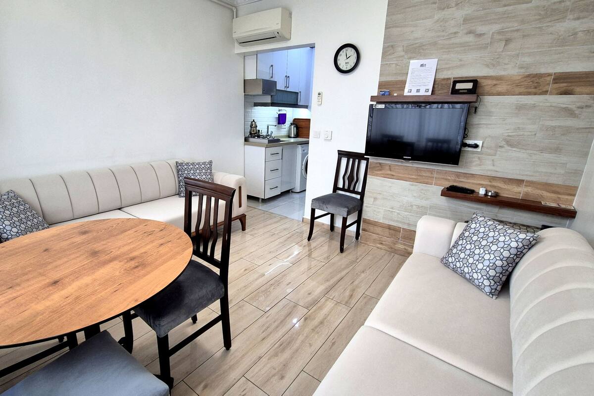 A modern living room with a sofa, a dining table, and a TV mounted on the wall.