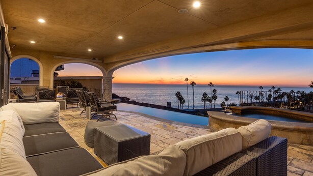 Zona de piscina con asientos y vista al océano al atardecer.