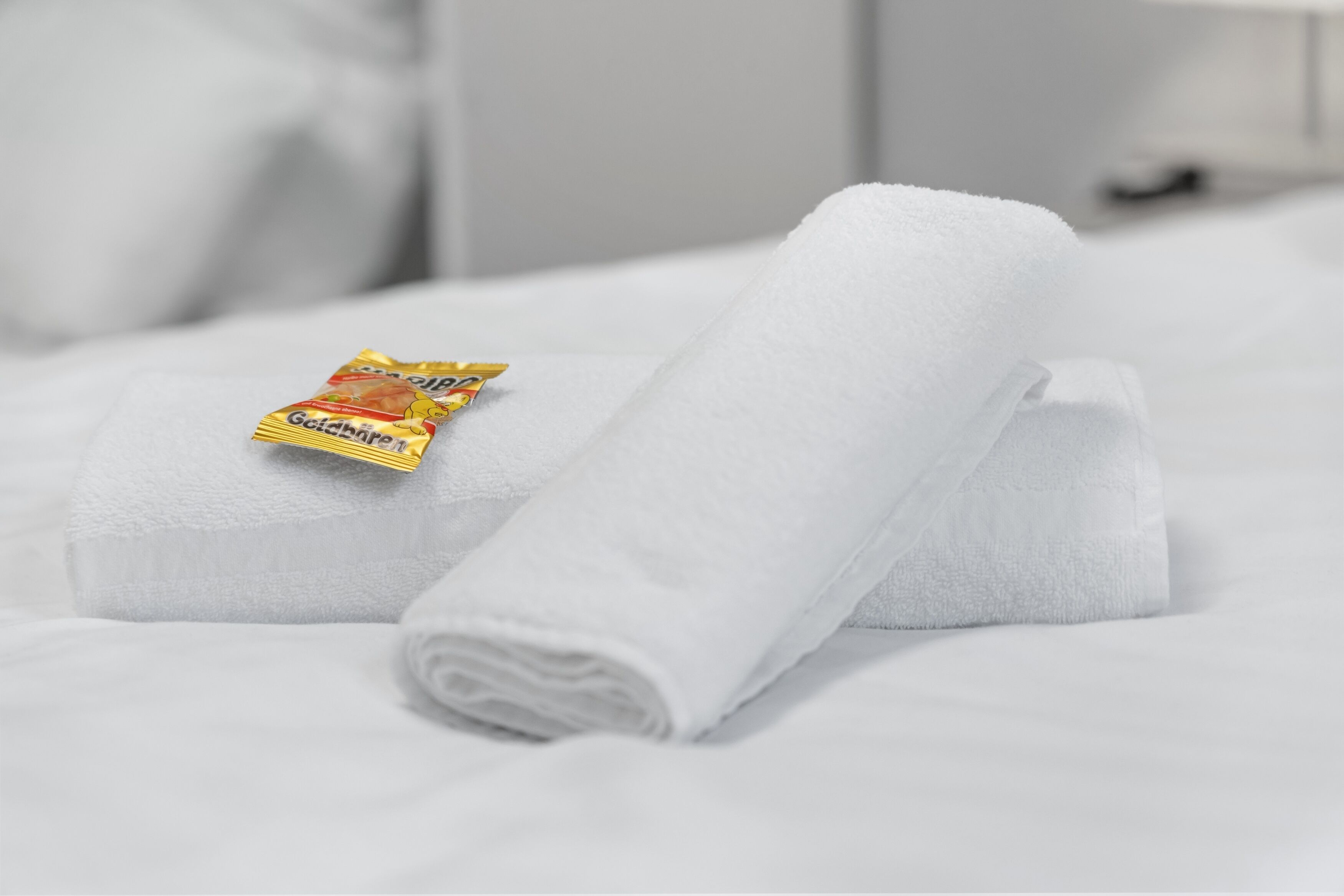 A neatly folded white towel and a packet of Goldbriand body lotion on a bed.